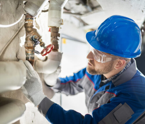Male Worker Inspecting Valve Male Worker Inspecting Water Valve For Leaks In Basement